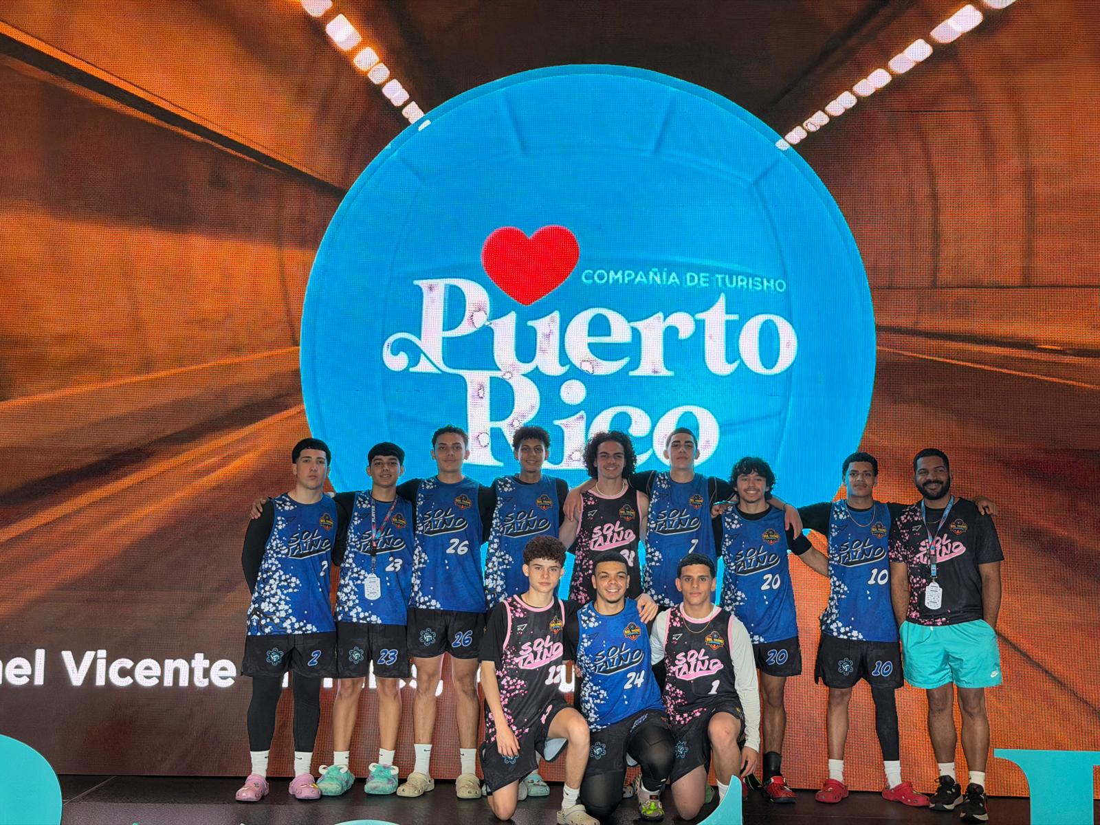 Equipo Sol Taíno en tarima frente al logo de la Compañía de Turismo de Puerto Rico